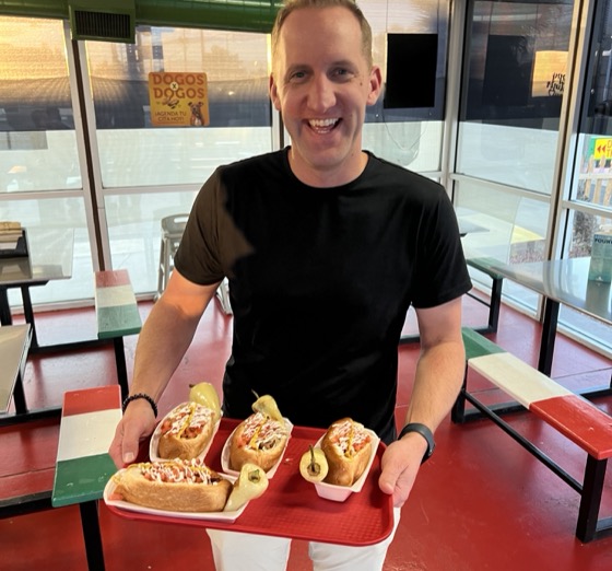 Photo of a handsome man holding a tray of delicious Sonoran Hot Dogs